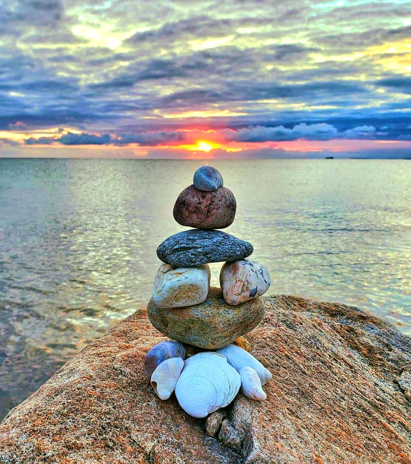Stacked stone cairn with shells against a dramatic ocean sunset